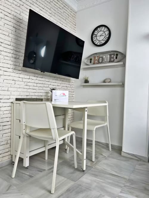 Moderno espacio de trabajo en apartamento de Fuengirola con escritorio blanco, sillas, pared de ladrillo y TV montada en pared