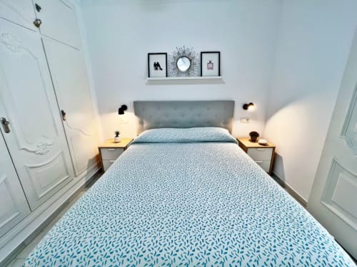 Moderno dormitorio con ropa de cama azul estampada, cabecero gris, mesitas de noche de madera y repisas en apartamento de Fuengirola