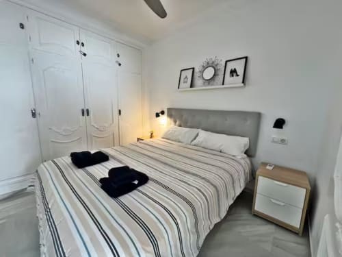 Dormitorio moderno en apartamento de playa en Fuengirola con ropa de cama rayada, cabecero gris, armarios empotrados blancos y diseño minimalista
