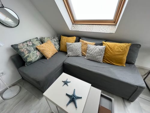 Sofá gris moderno en forma de L con cojines amarillos en apartamento junto al mar, Fuengirola, bajo tragaluz