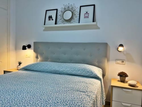 Dormitorio moderno con cabecero azul claro, ropa de cama estampada, repisa decorativa e iluminación cálida en apartamento de Fuengirola