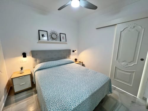 Dormitorio moderno en apartamento frente al mar en Fuengirola con cabecero tapizado gris, ropa de cama azul estampada y diseño contemporáneo