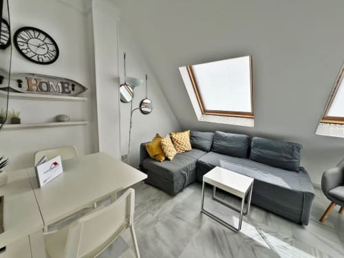Moderno apartamento ático en Fuengirola con sofá seccional gris, ventanas cenital y decoración minimalista