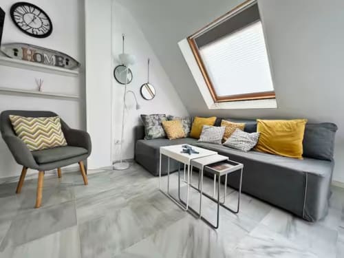 Moderno salón de apartamento con sofá gris, detalles en amarillo y claraboya en Fuengirola