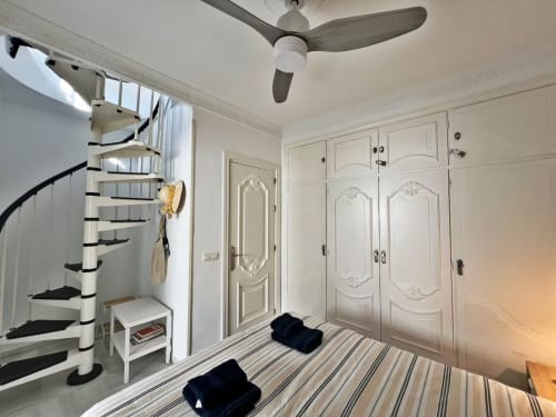 Dormitorio de apartamento en Fuengirola con escalera de caracol, armario blanco, ventilador de techo y suelo a rayas