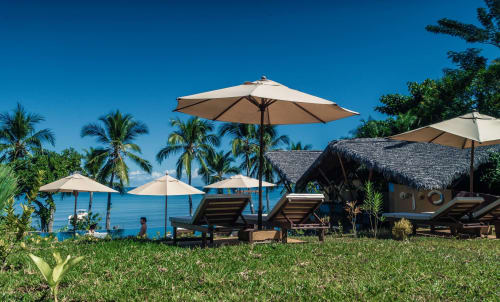 Plage du lodge Belamandy à Nosy Be avec parasols, chaises longues, bungalows en chaume et palmiers