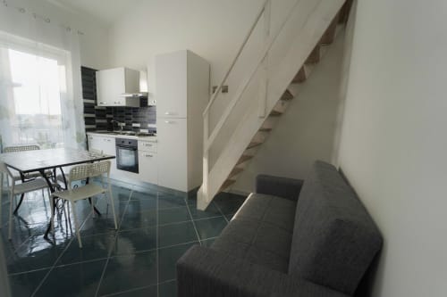 Moderna cucina e zona living con tavolo da pranzo, divano grigio e scala nell'appartamento Antico Palazzo del Corso a Mirto