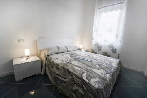 Camera luminosa dell'appartamento Levante ad Antico Palazzo del Corso con letto queen, comodino bianco, lampada e finestra con vista su verde