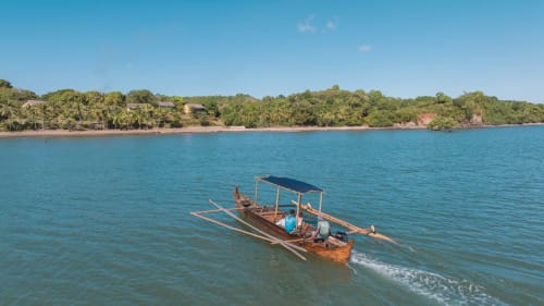 Bateau en bois traditionnel ancré dans les eaux turquoise de Nosy Be, avec la forêt tropicale luxuriante du lodge Belamandy en arrière-plan