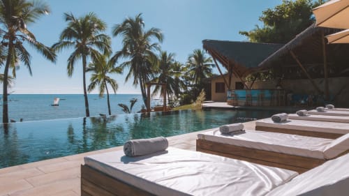 Piscine à débordement du Belamandy Lodge avec vue sur l'océan, palmiers et chaises longues surplombant Nosy Bé, Madagascar