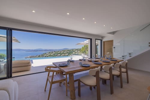 Villa de luxe avec salle à manger vue mer, table en bois, cuisine moderne et baies vitrées panoramiques sur la Méditerranée