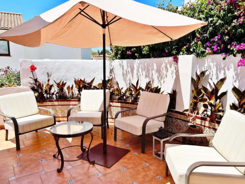 Terraza soleada con zona de descanso, sombrilla beige y plantas floridas con vistas al jardín de Fuengirola