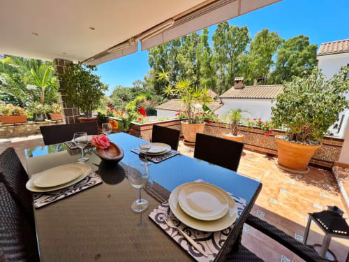 Terraza soleada con comedor en apartamento de Fuengirola, vistas al jardín, plantas en macetas y decoración estilo mediterráneo
