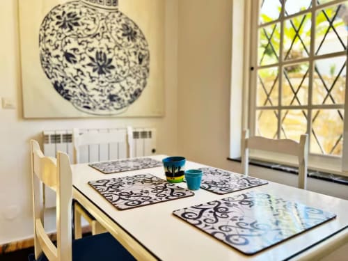 Luminoso comedor en apartamento de Fuengirola con salvamanteles decorados, taza turquesa y vistas al jardín por ventanas enrejadas