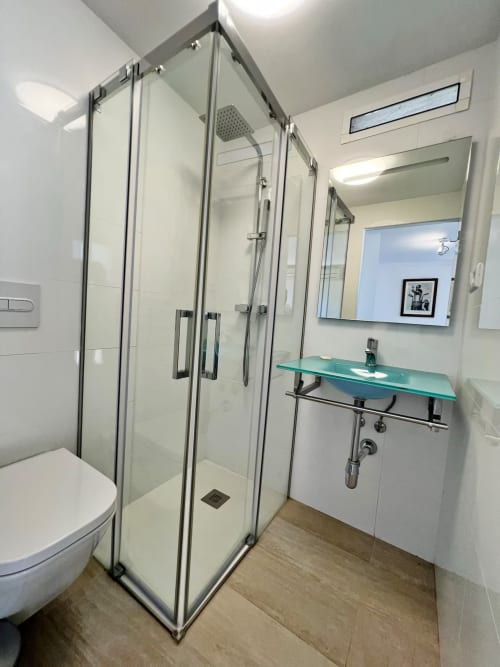 Baño moderno en apartamento de Fuengirola con ducha de cristal, lavamanos turquesa e iluminación brillante