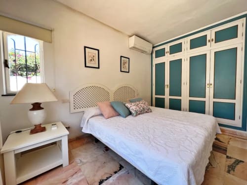 Dormitorio luminoso con cama de matrimonio, armario turquesa y vistas al jardín en apartamento de Fuengirola