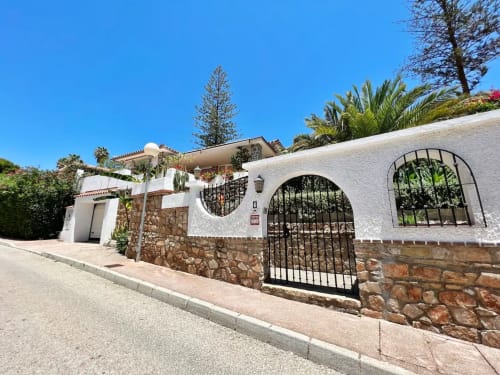 Villa mediterránea blanca con base de piedra en Fuengirola, con entrada arqueada y vistas al jardín de palmeras