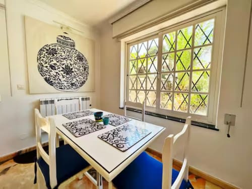 Luminoso apartamento independiente en Fuengirola con mesa de comedor, cuadros con motivos negros y vistas al jardín a través de celosía
