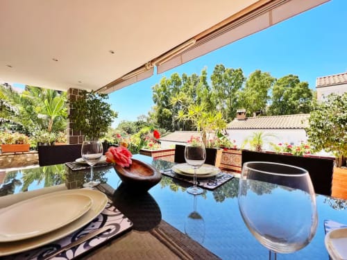 Elegante comedor al aire libre en terraza con vistas al jardín, copas de vino y mesa preparada en apartamento de Fuengirola