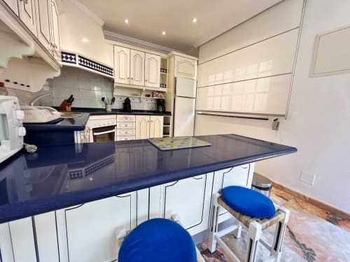 Cocina moderna con isla azul marino y taburetes azules, muebles crema, apartamento en Fuengirola