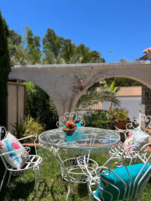 Mobiliario blanco ornamentado con cojines turquesas en soleado jardín, puente de arco de piedra, apartamento en Fuengirola