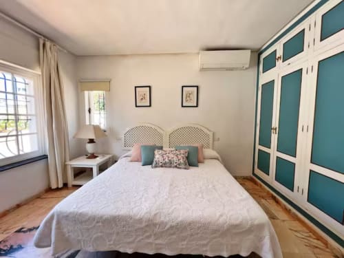 Dormitorio luminoso en apartamento de Fuengirola con cama queen, armario turquesa, vista al jardín y comodidades modernas