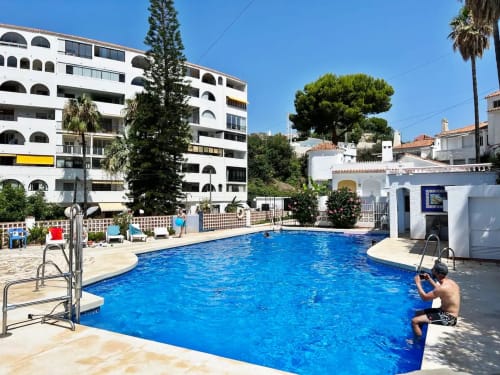 Zona de piscina luminosa en Fuengirola con agua azul, tumbonas y modernos edificios blancos rodeados de jardines