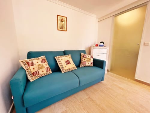 Acogedora sala de estar en Fuengirola con sofá turquesa, cojines decorativos, suelos de madera y puerta amarilla brillante.