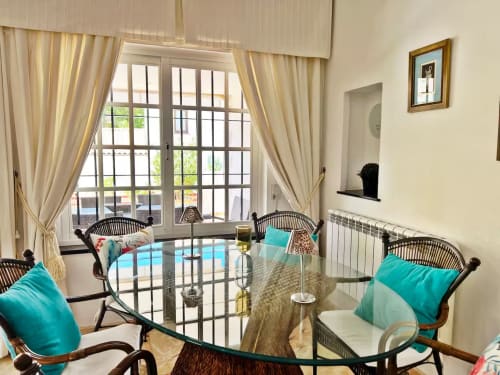 Luminoso apartamento en Fuengirola con acentos turquesas, mesa de cristal, sillas de mimbre y vistas al jardín