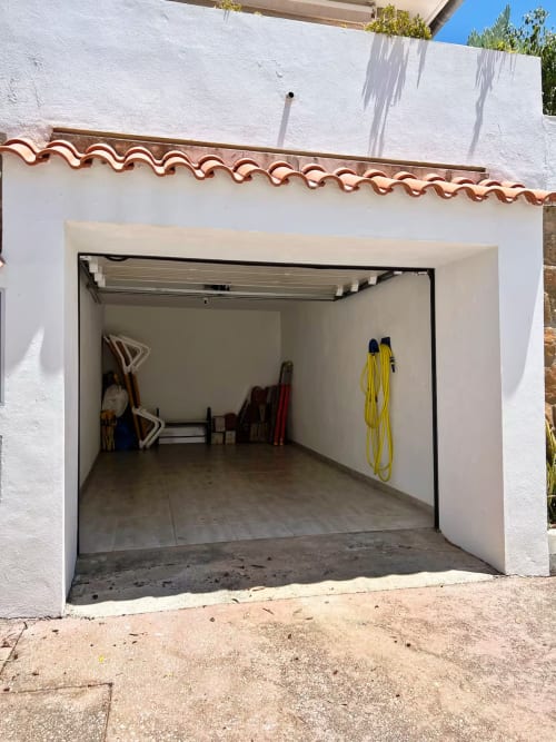 Garaje vacío con paredes blancas y techo de barro en apartamento de Fuengirola, almacenando manguera amarilla y herramientas
