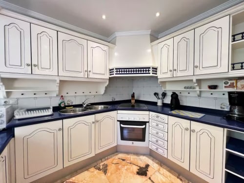 Cocina moderna con muebles color crema, encimeras oscuras y azulejos decorativos en apartamento de Fuengirola
