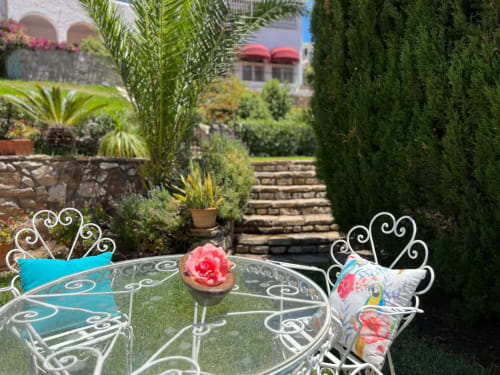 Muebles de jardín de hierro forjado con rosa rosa que domina el exuberante jardín del apartamento de Fuengirola con palmeras y setos de ciprés