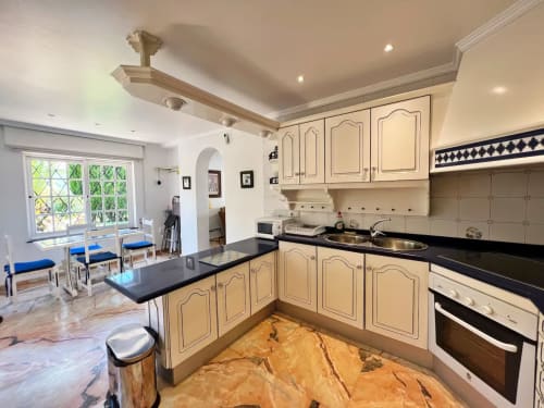 Cocina moderna color crema con encimeras negras y fregadero de acero inoxidable en luminoso apartamento de Fuengirola con vistas al jardín