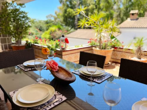 Zona de comedor al aire libre en apartamento de Fuengirola con mesa servida, flores y vistas al jardín desde la terraza