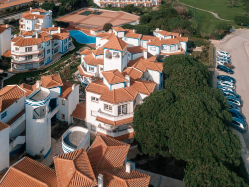Vista aérea do hotel Be SilverCoast em Serra D'El Rei com edifícios brancos e azuis, telhados em terracota e piscina compartilhada