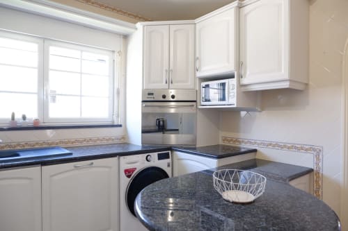 Cozinha moderna da Casa Lusitania no hotel Be SilverCoast, Serra D'El Rei, com armários brancos e bancadas em granito preto