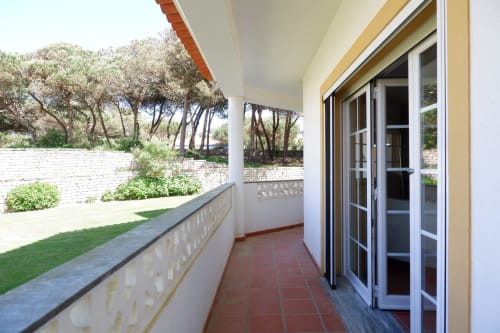 Terraço coberto com piso de azulejos vermelhos na Casa Lusitania, hotel Be SilverCoast em Serra D'El Rei, com vista para o jardim e pinheiros