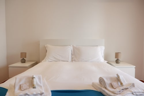 Quarto claro na Be SilverCoast Casa Lusitania com roupa de cama branca, almofadas, duas mesas-de-cabeceira com abajures e paredes bege