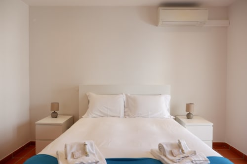 Quarto minimalista no hotel Be SilverCoast em Serra D'El Rei com cama branca, paredes neutras, ar condicionado e criado-mudo