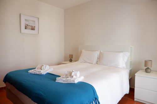 Quarto claro e arejado do hotel Be SilverCoast em Serra D'El Rei com camas de solteiro, lençol branco, manta azul e decoração minimalista