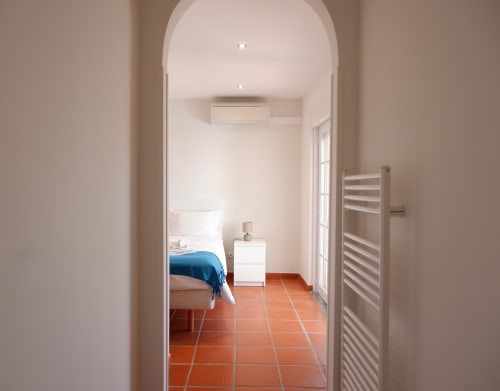 Quarto moderno em Be SilverCoast com entrada em arco, roupa de cama azul, criado-mudo branco, piso de cerâmica terracota e ar condicionado