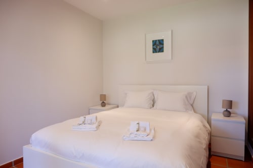 Quarto minimalista no hotel Be SilverCoast com roupa de cama branca, mesas laterais e obra de arte azul na parede