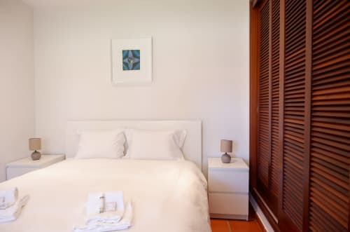 Quarto claro no Be SilverCoast com cama branca, luminárias de cabeceira e guarda-roupa em madeira na suíte Casa Lusitania