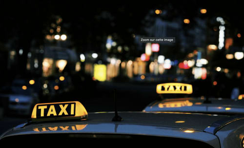 Yellow taxi roof lights illuminated at night with blurred city lights in background, Tincave Bozel