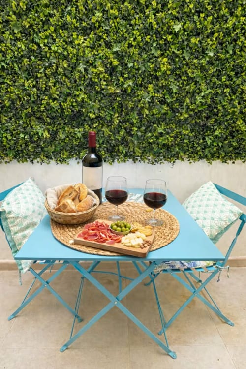 Mesa azul al aire libre con vino, tabla de embutidos y pan, rodeada de exuberante vegetación en Grupo Inmo House Fuengirola