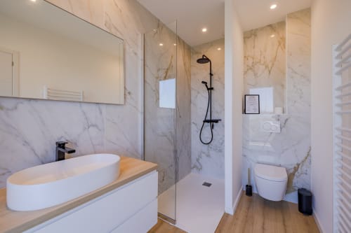 Salle de bain moderne en marbre de la Villa Prestige Azur Antilles avec lavabo ovale blanc, douche vitrée et toilettes