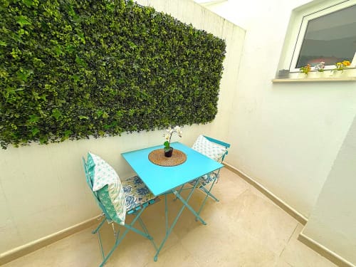 Soleado patio de apartamento en la playa de Fuengirola con mesa turquesa, sillas acolchadas verdes y muro vegetal exuberante
