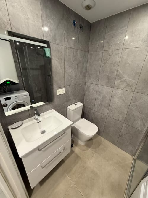 Baño moderno con azulejos grises, lavamanos blanco, inodoro y cabina de ducha en apartamento de playa en Fuengirola