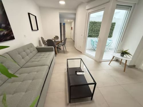 Luminoso apartamento moderno en primera línea de playa en Fuengirola con sofá gris, comedor y acceso a terraza por amplias puertas de cristal