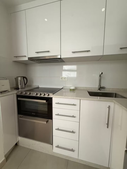 Cocina moderna blanca con electrodomésticos de acero inoxidable en luminoso apartamento de playa en Fuengirola